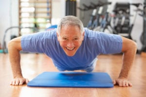 Senior Man Doing Press Ups In Gym Smiling To Camera