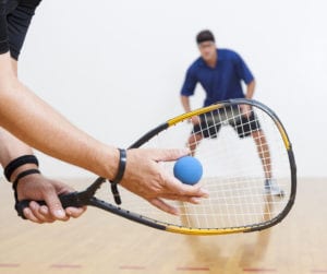 Two men playing racquetball on court. One serving.