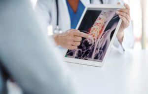 A spine doctor holding up a tablet and showing an image of a spine to a patient who is about to undergo treatment.