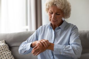 An elderly woman holding her wrist due to the pain she's having from arthritis since she hasn't had treatment.