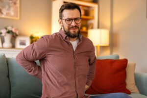 Young man experiencing sharp lower back pain and Sciatica pain after long hours of sitting.