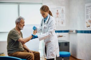 Female orthopedic doctor examining hand of a senior patient with arthritis pain at medical clinic.