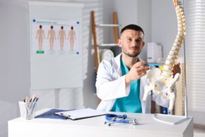 Doctor with human spine model in hospital to explain sciatica pain to a patient.